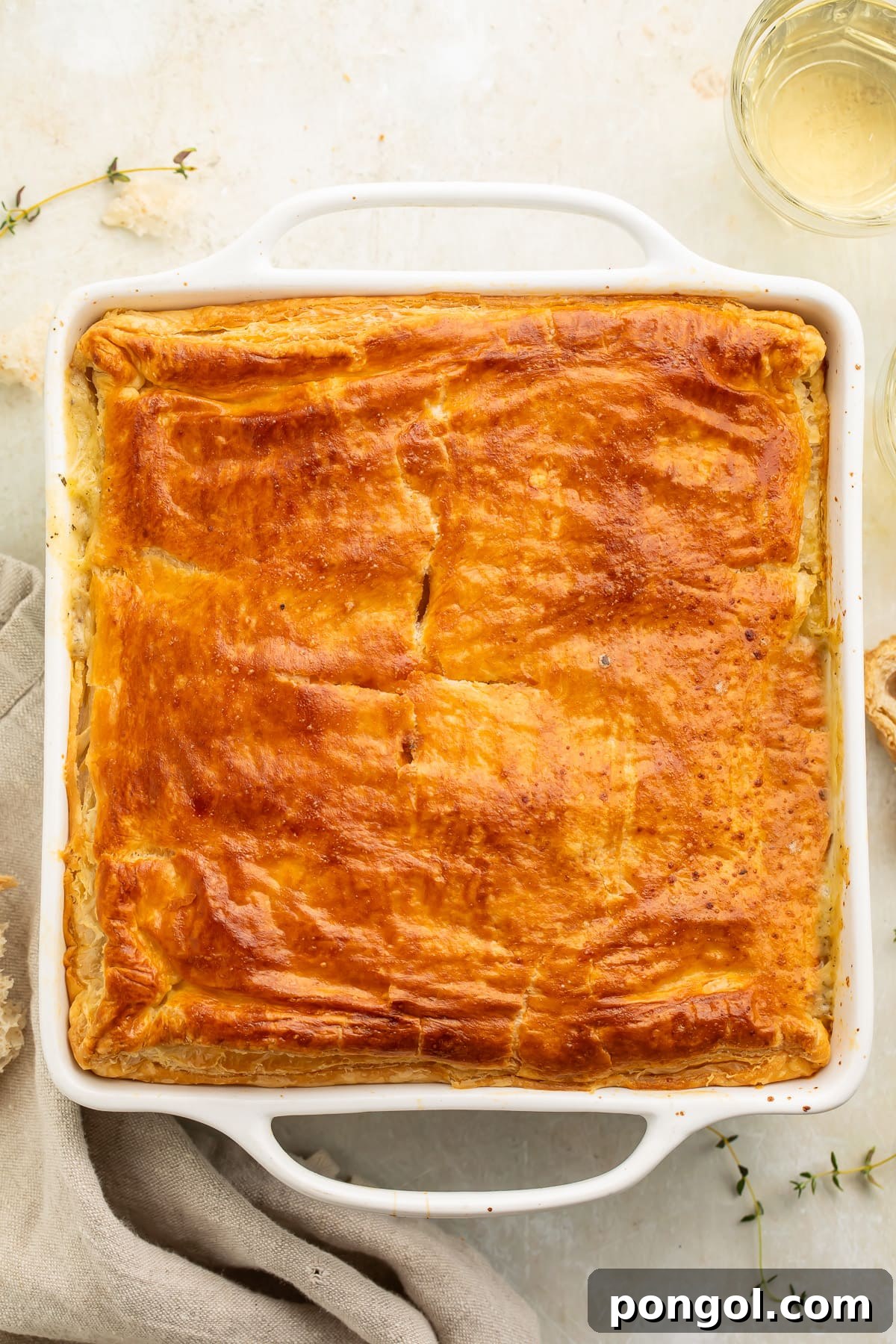 Comforting Chicken Pot Pie Bake 3 An overhead shot of a bubbling chicken pot pie casserole in a square baking dish, with the golden puff pastry crust slightly puffed and browned.