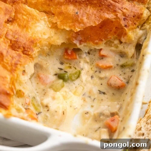 Chicken pot pie casserole in a square dish, with a corner scooped out to show some of the filling.