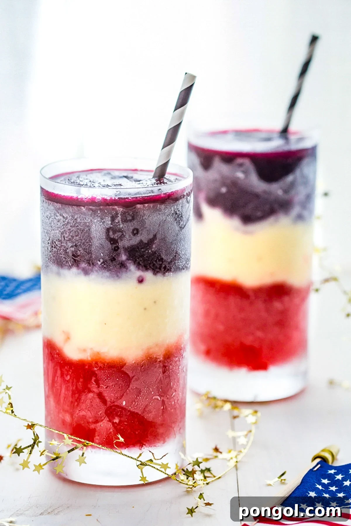 Two tall glasses containing vibrant red, white, and blue layered paleo cocktails, perfect for 4th of July celebrations.