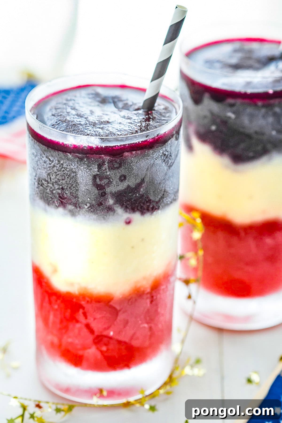 Two tall glasses containing red, white, and blue layered cocktails, garnished with fresh fruit, ready to be enjoyed.