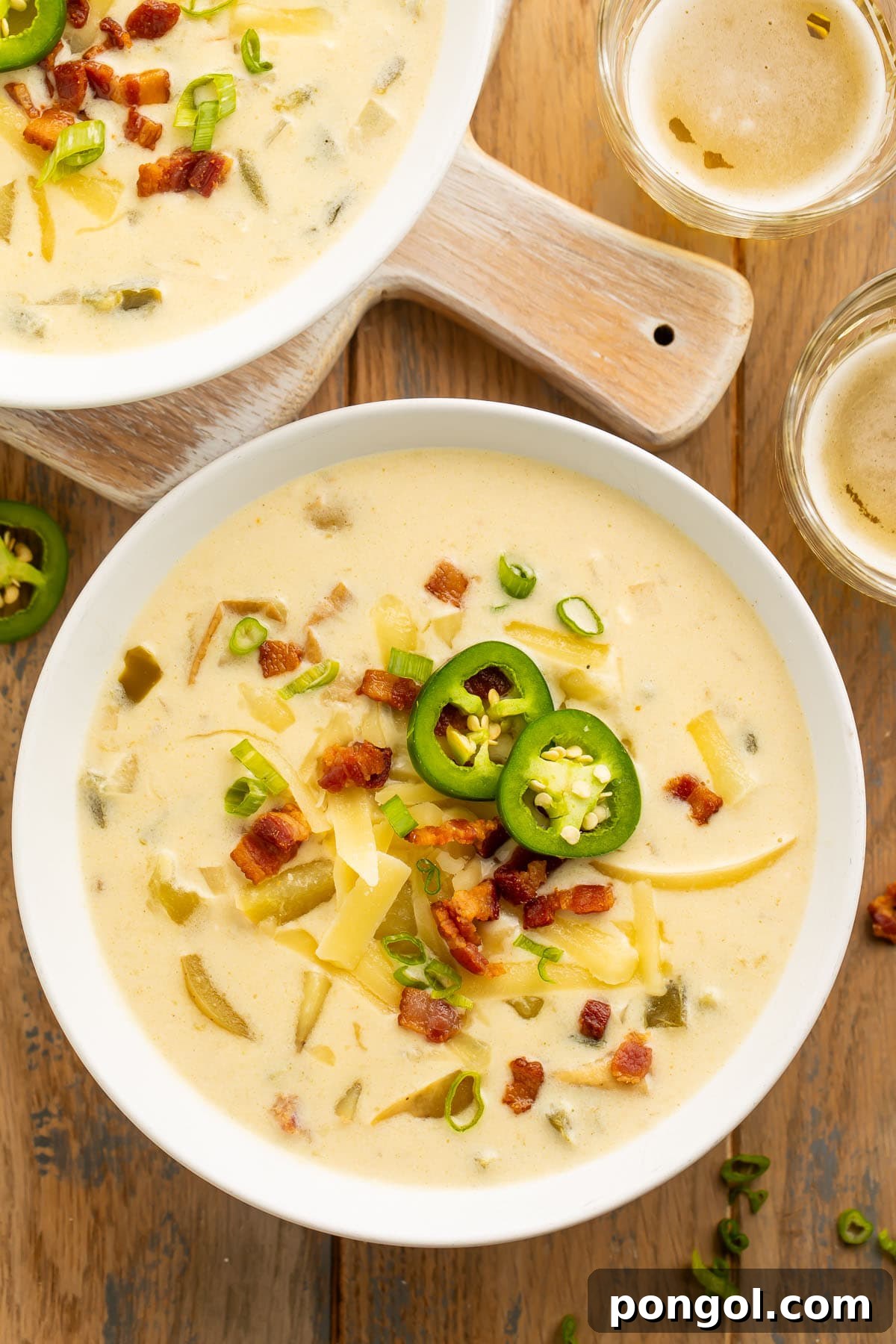 Overhead view of 2 large white bowls holding pale yellow jalapeño popper soup on a wooden table.