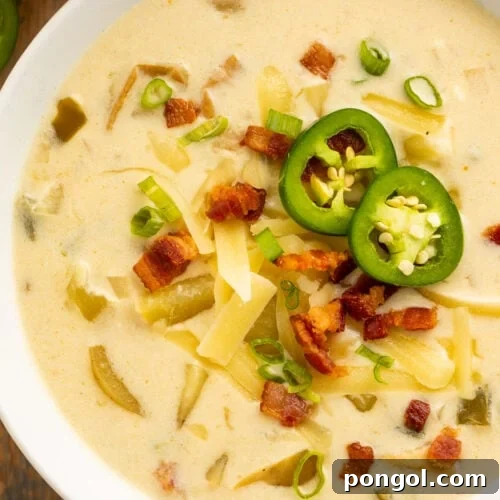 Top-down view of a large white bowl holding pale yellow, creamy jalapeño soup, topped with sliced jalapeños, diced bacon, and shredded cheese.
