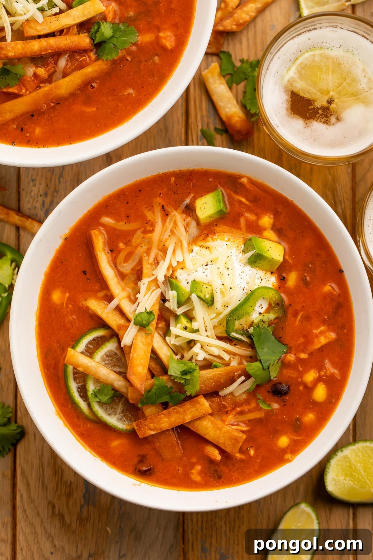 Overhead photo of a large white bowl holding deep red chicken tortilla soup, made in an Instant Pot, topped with tortilla strips, cheese, avocado, and cilantro.