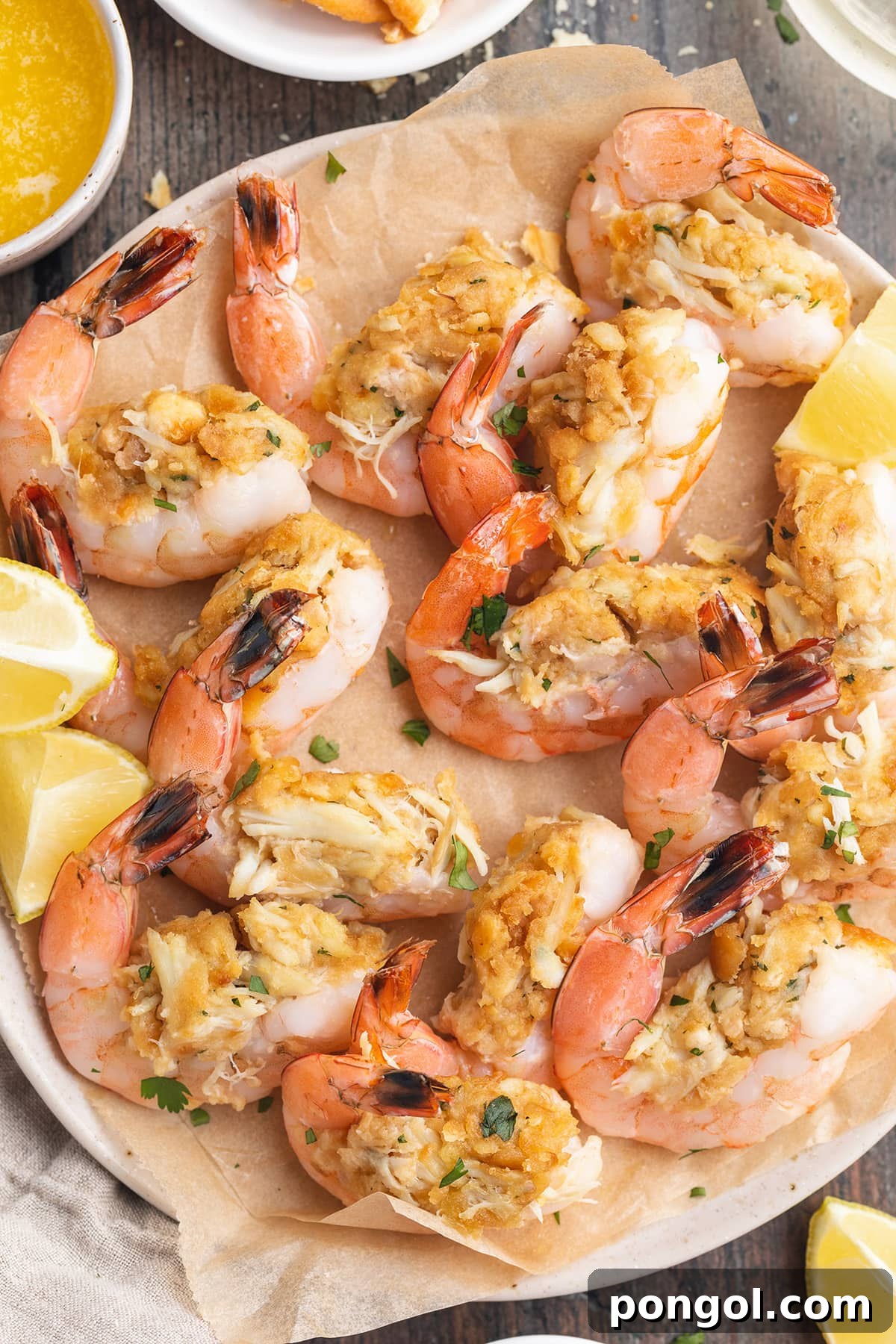 Top-down photo of a plate of baked, stuffed shrimp with vibrant lemon wedges and fresh green herbs, showcasing the golden-brown crust of the stuffing.