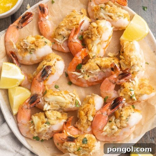 Top-down photo of a plate of baked, stuffed shrimp with lemon wedges and fresh herbs.
