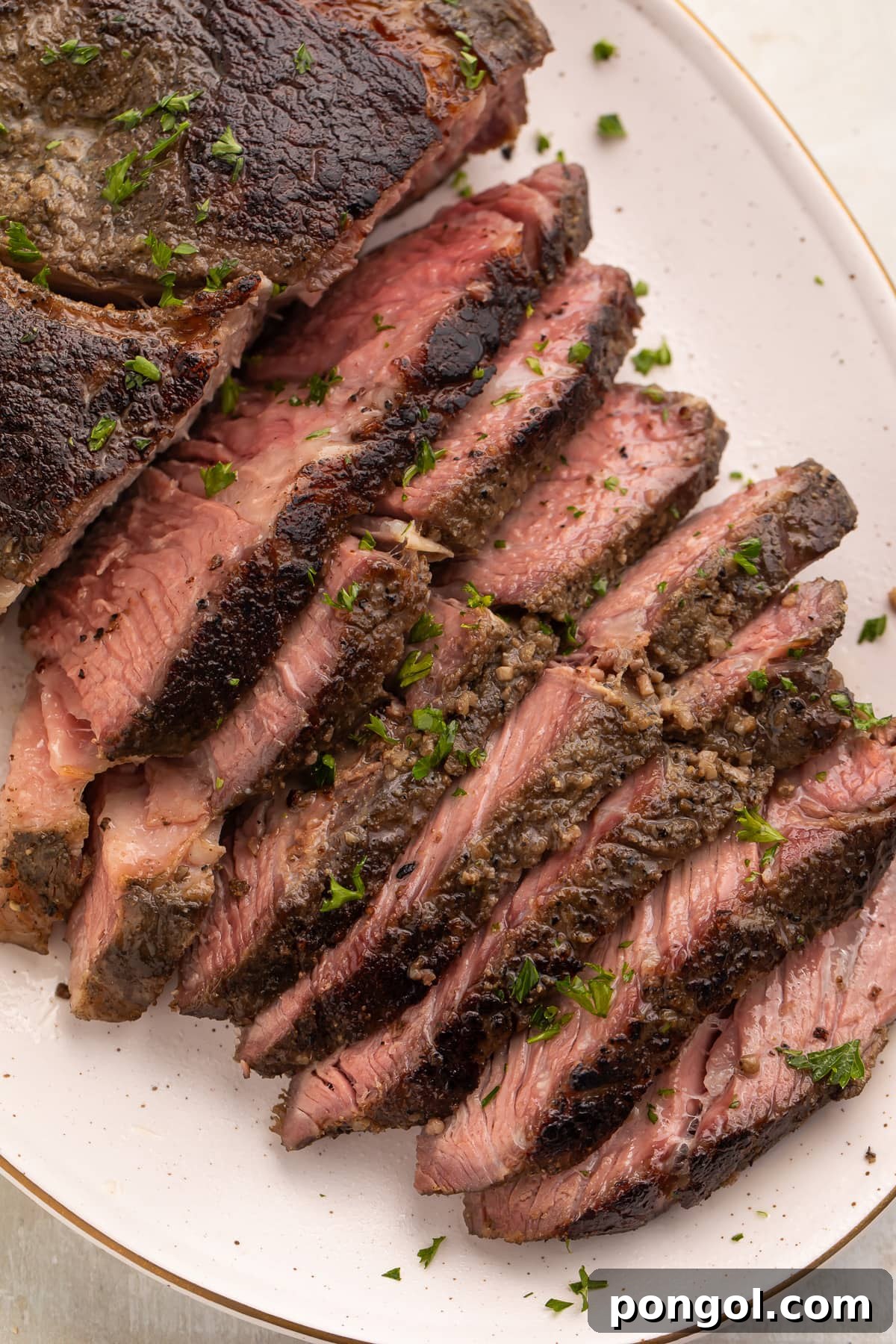 Overhead photo of sous vide chuck roast on a white platter, with half the chuck roast sliced into thin strips and fanned out to show the crust and the inside of the roast.