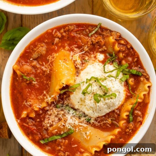 A bowl of lasagna soup on a wooden table next to a piece of bread and a glass of wine.