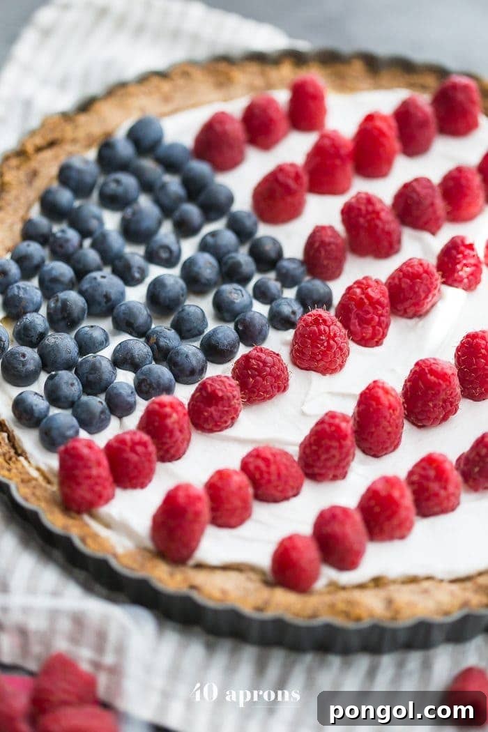 A vibrant Paleo Flag Fruit Tart with a golden crust, white coconut cream, and fresh blueberries and raspberries arranged like an American flag, ready for Fourth of July celebrations.