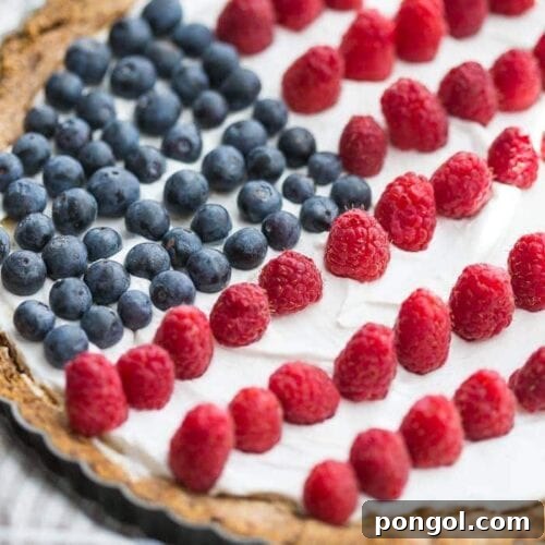 A beautifully decorated Paleo Flag Fruit Tart, featuring fresh blueberries and raspberries on a creamy white topping, perfect for a healthy Fourth of July dessert.