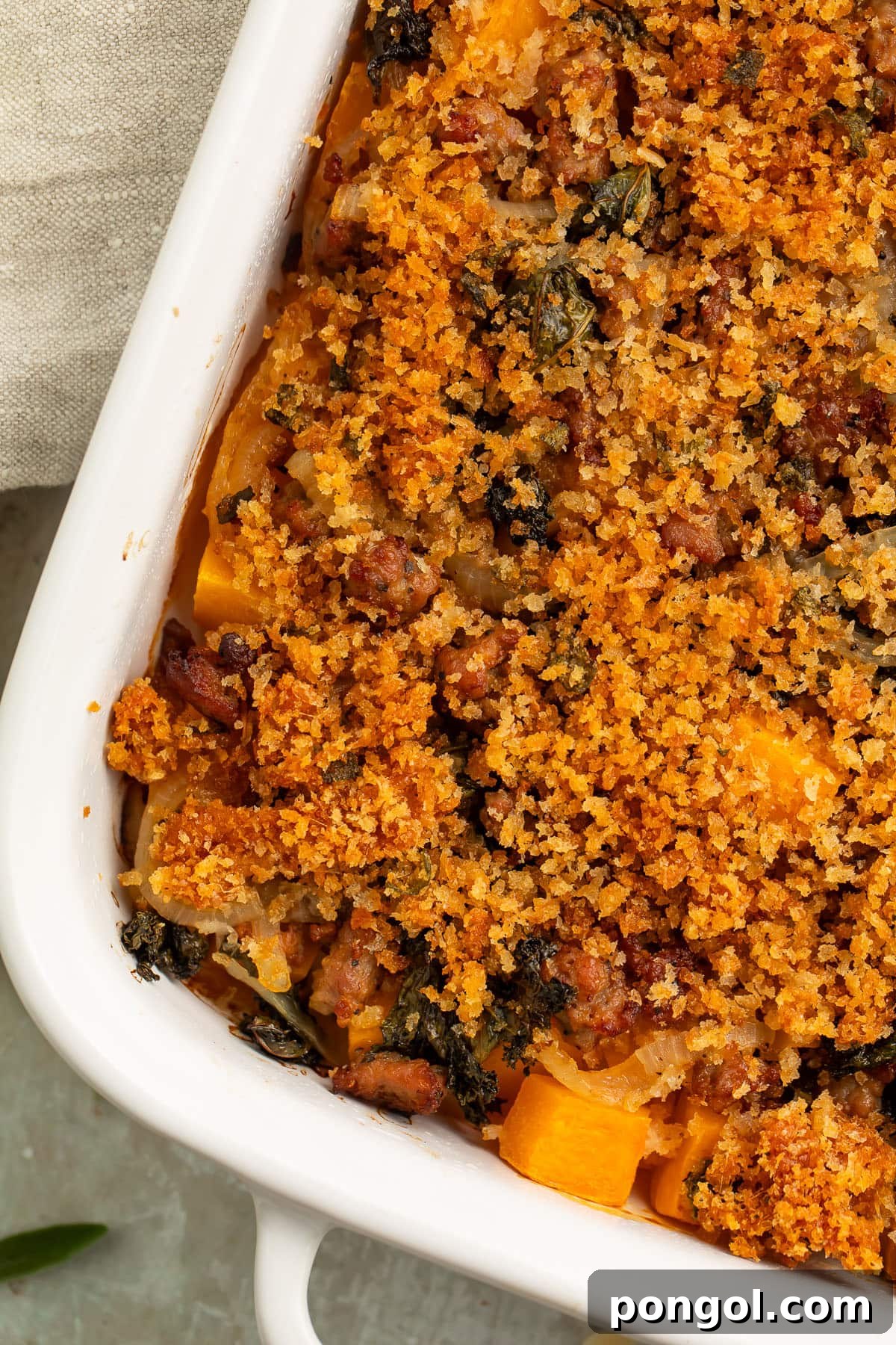 30 Festive Casseroles Your Holiday Table Needs 16 Overhead view of a large white casserole dish, angled on a table, holding a butternut squash casserole topped with breadcrumbs.