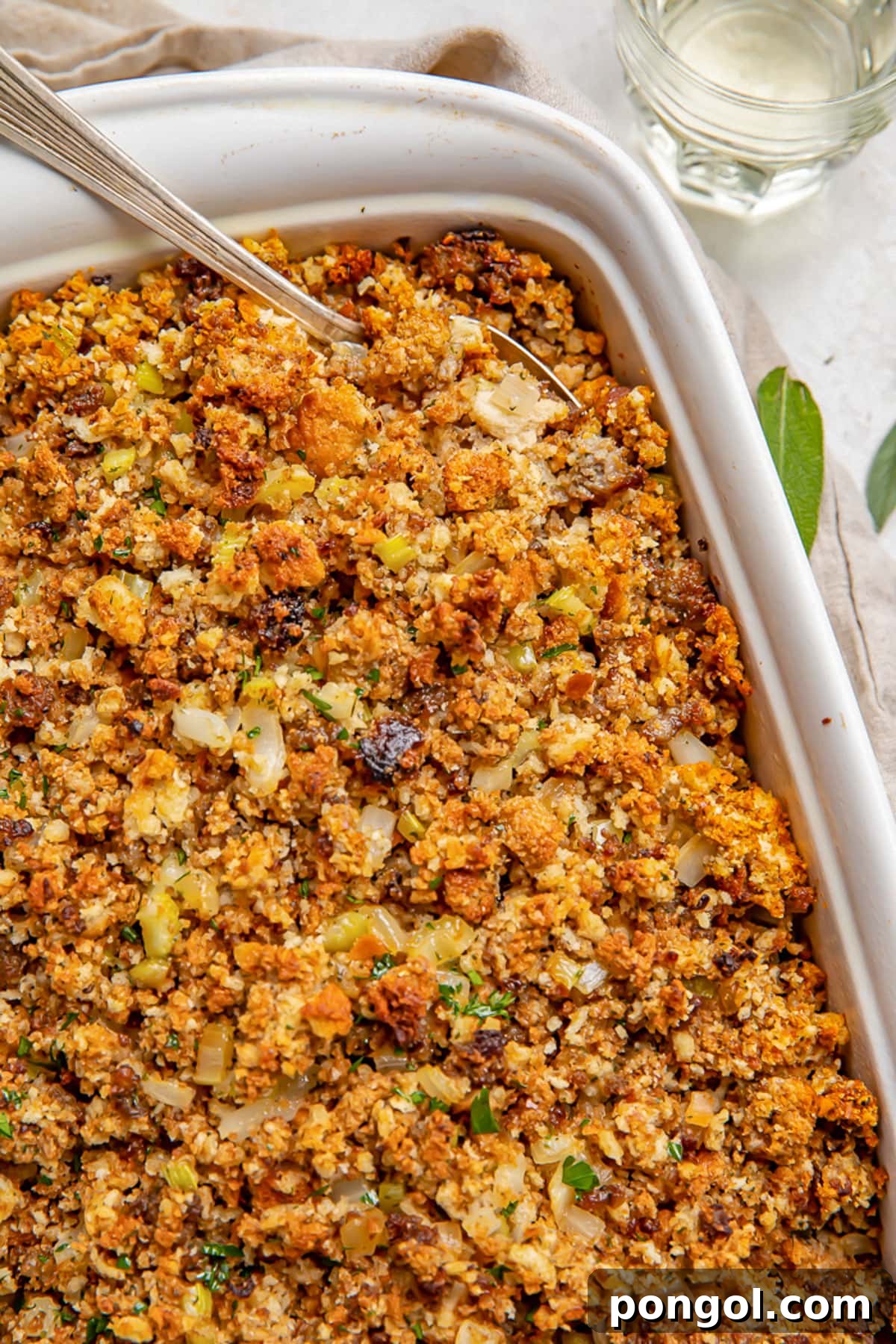 30 Festive Casseroles Your Holiday Table Needs 17 Sausage stuffing in a white rectangular casserole dish with a large spoon.