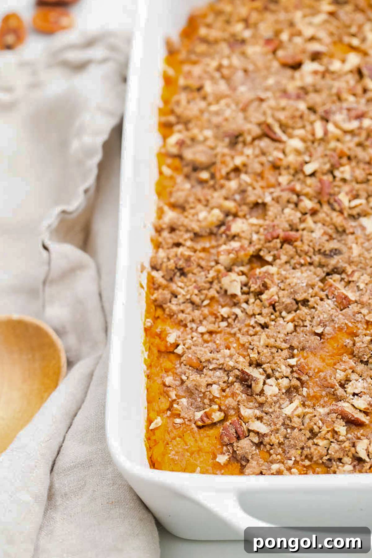30 Festive Casseroles Your Holiday Table Needs 28 A large white rectangular casserole dish holding sweet potato casserole topped with pecans.