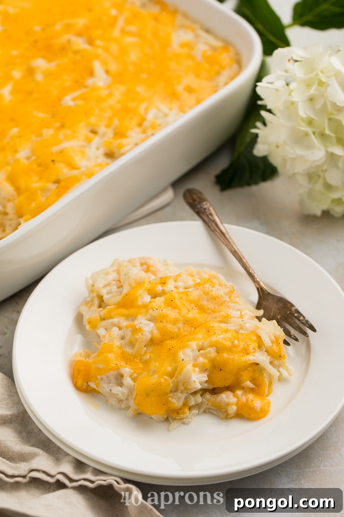 30 Festive Casseroles Your Holiday Table Needs 8 Closer, angled view of a scoop of Cracker Barrel hashbrown casserole topped with cheese on a white plate with a fork.