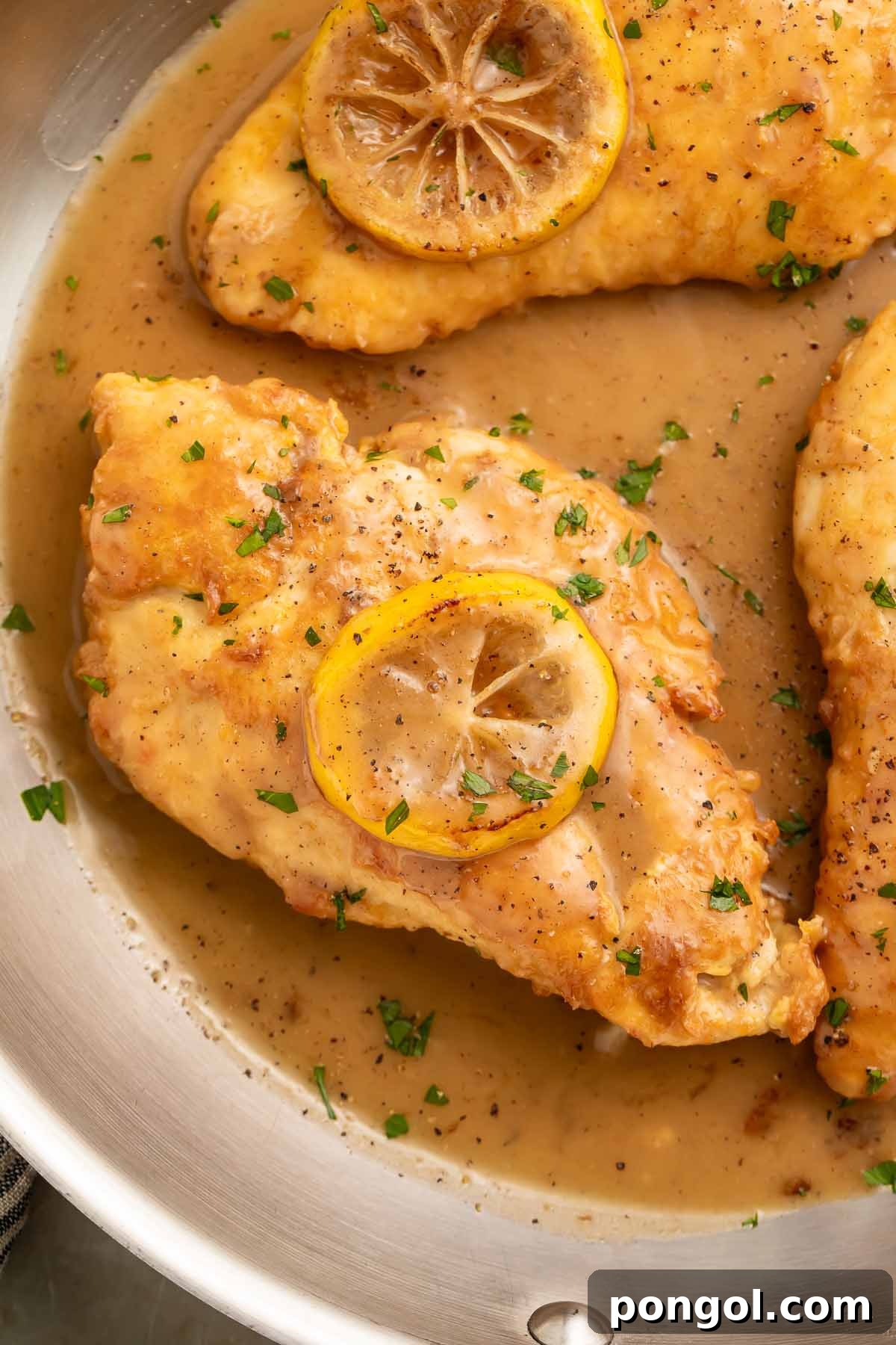 Lightly pan-fried Chicken Francese simmering in a large skillet, coated in a glistening lemon sauce, beautifully garnished with a sautéed lemon coin.