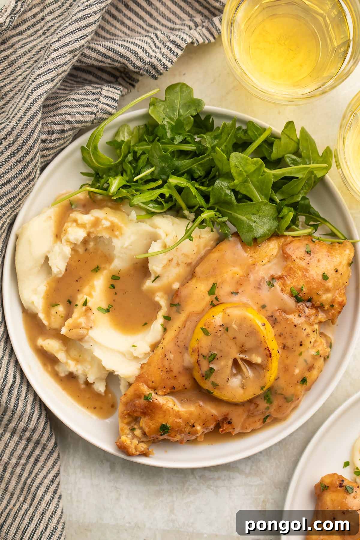 A perfectly plated serving of Chicken Francese with creamy mashed potatoes and a vibrant small green leafy salad on a white dish.