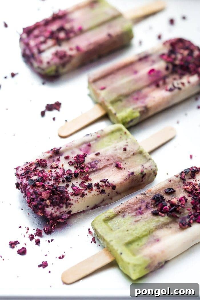 Layered mermaid popsicles featuring green matcha, white coconut, and purple roasted blackberry swirls, perfect for a summer treat.