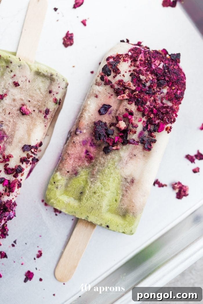 Close-up of a mermaid popsicle showcasing vibrant layers of green matcha, creamy white coconut, and swirling roasted blackberries.