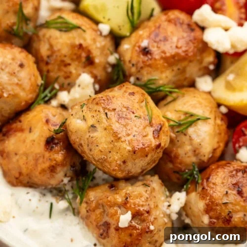 Close-up of Greek chicken meatballs in a large bowl with rice and veggies, ready to be served.