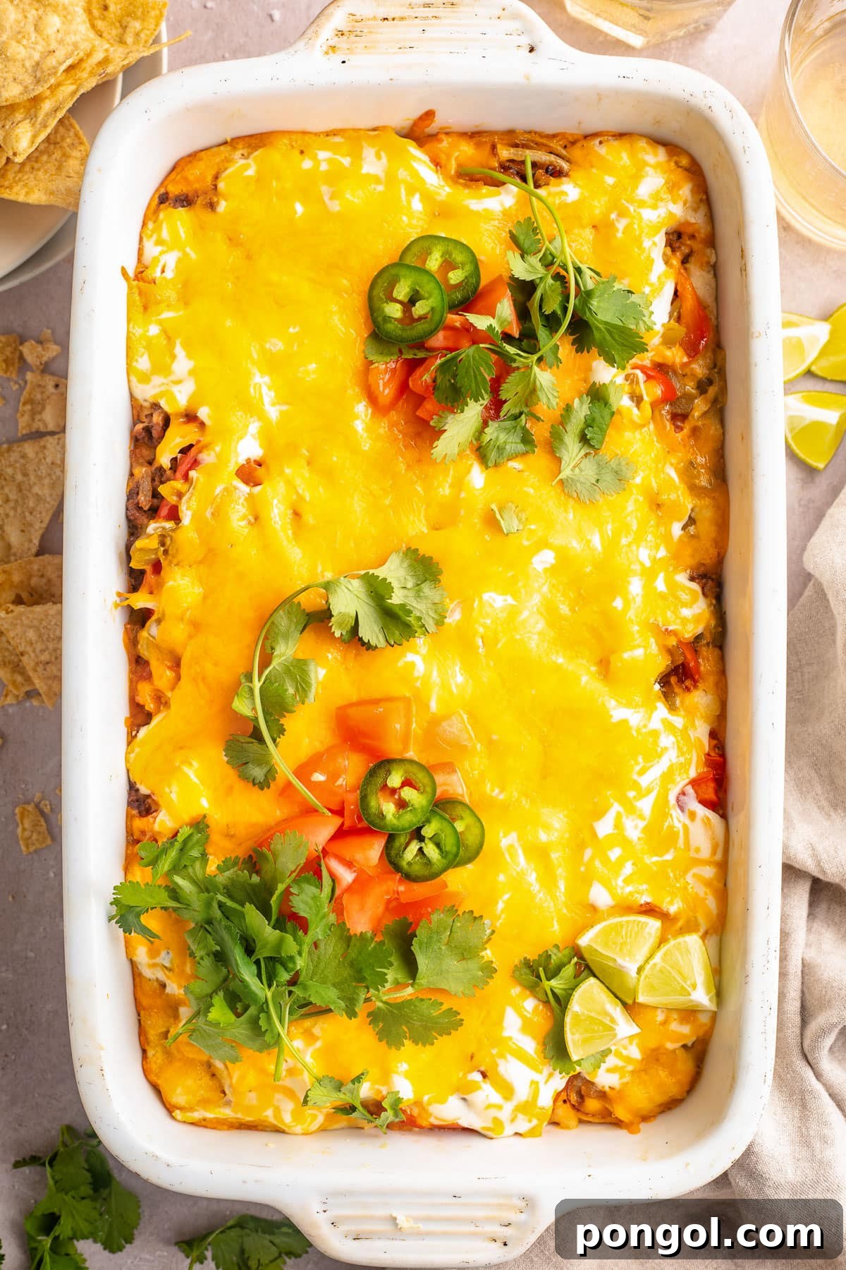 Overhead view of a large white rectangular casserole dish holding John Wayne casserole topped with melted cheese, tomatoes, jalapeño slices, and cilantro. A classic hearty meal for any occasion.