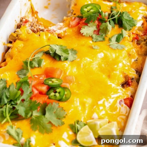 Overhead view of a large white rectangular casserole dish holding John Wayne casserole topped with melted cheese, tomatoes, jalapeño slices, and cilantro.