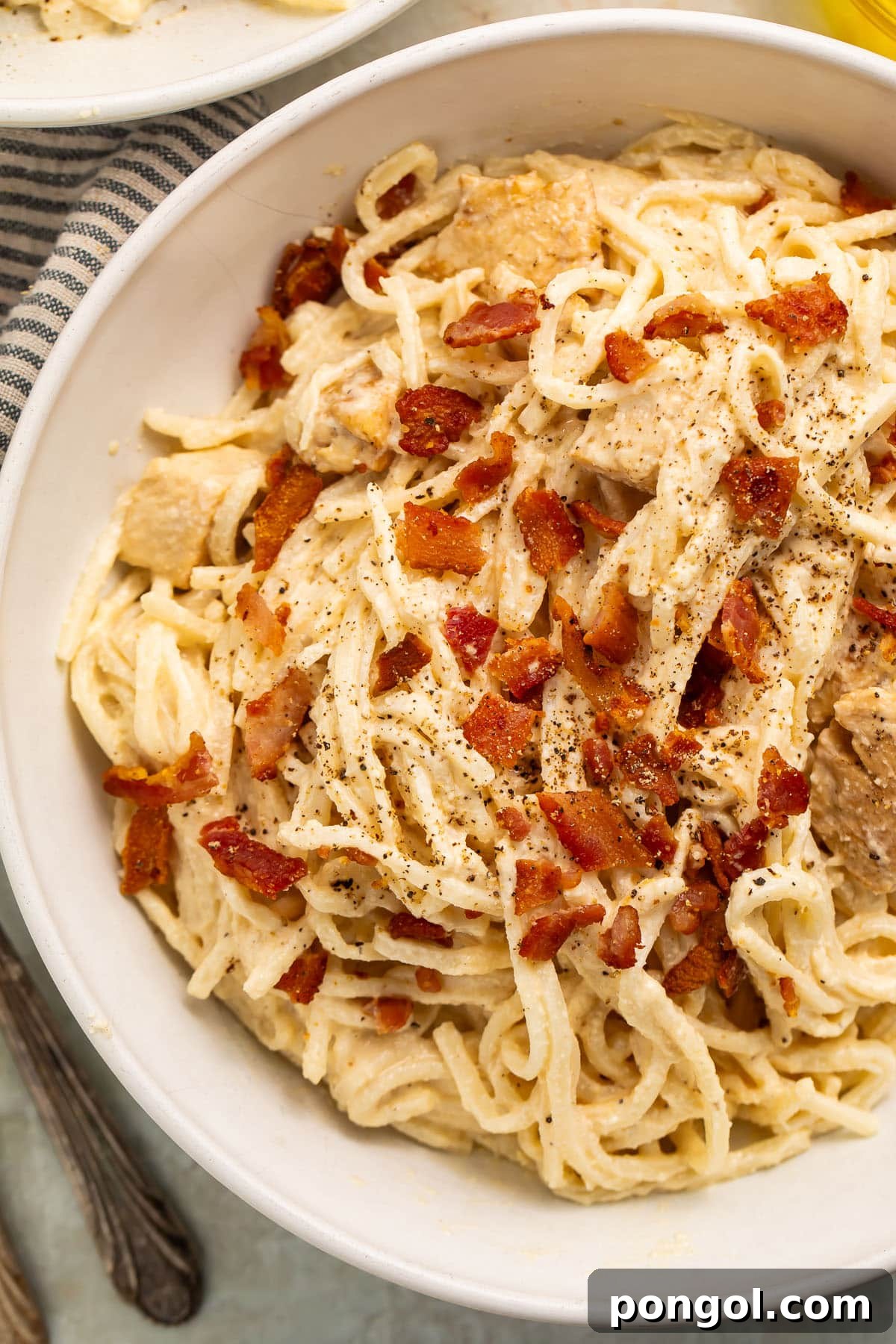 A large white bowl of paleo carbonara made with palmini, dairy-free Alfredo sauce, and compatible bacon, with a fork digging in.