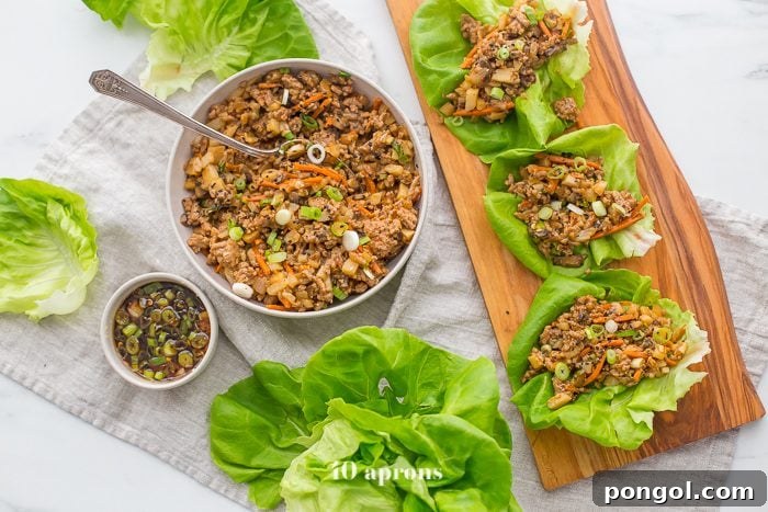 A selection of healthy PF Changs inspired lettuce wraps on a board, with a side bowl of the savory filling and fresh lettuce leaves for assembly.