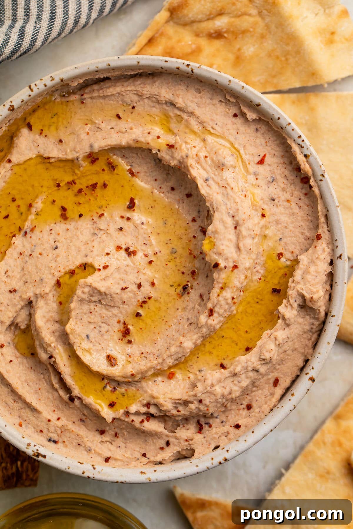 A beautifully swirled bowl of black eyed pea hummus, generously drizzled with high-quality olive oil and garnished with fresh green herbs. The lighting is bright and inviting, showcasing the smooth texture and appealing color of the dip.