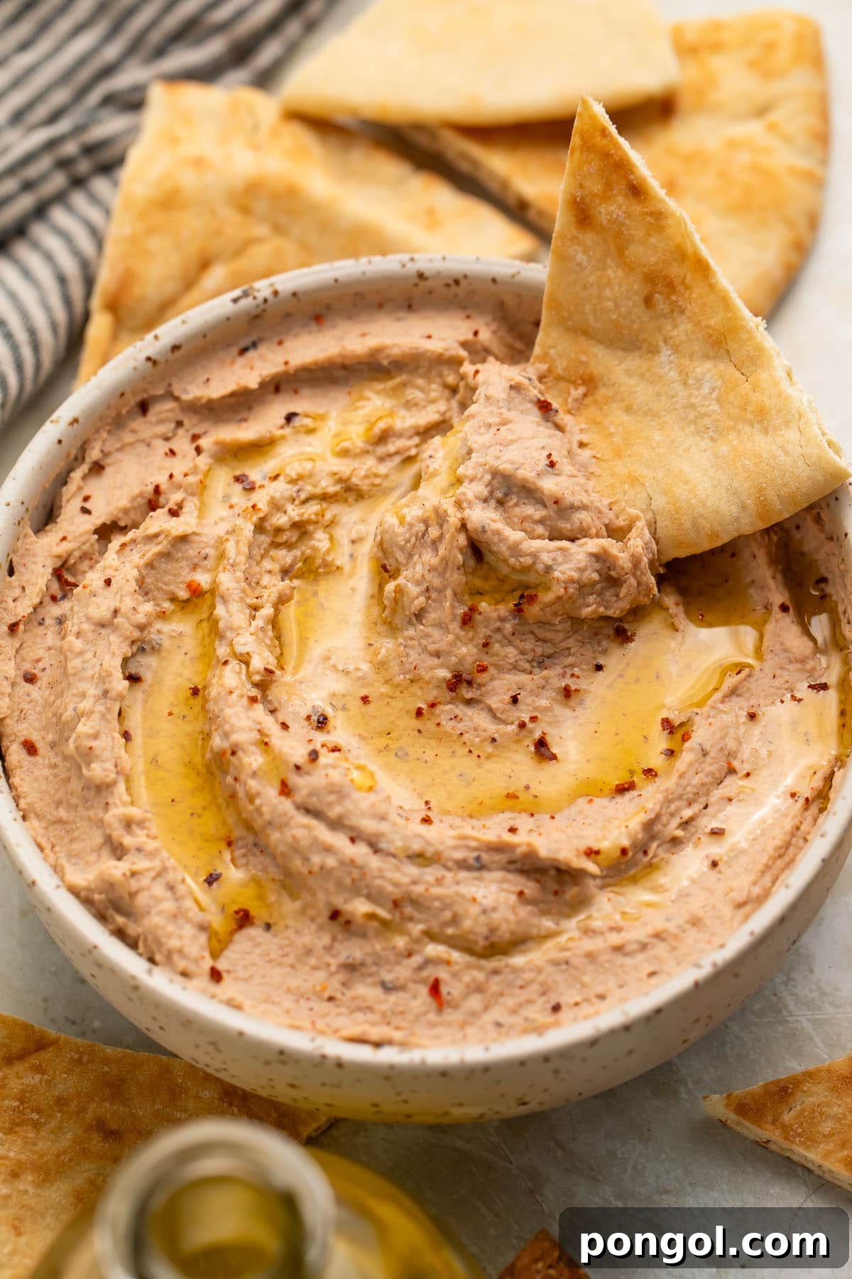 A close-up shot of a triangular pita chip perfectly scooped with a generous portion of creamy black eyed pea hummus, showcasing its inviting texture.