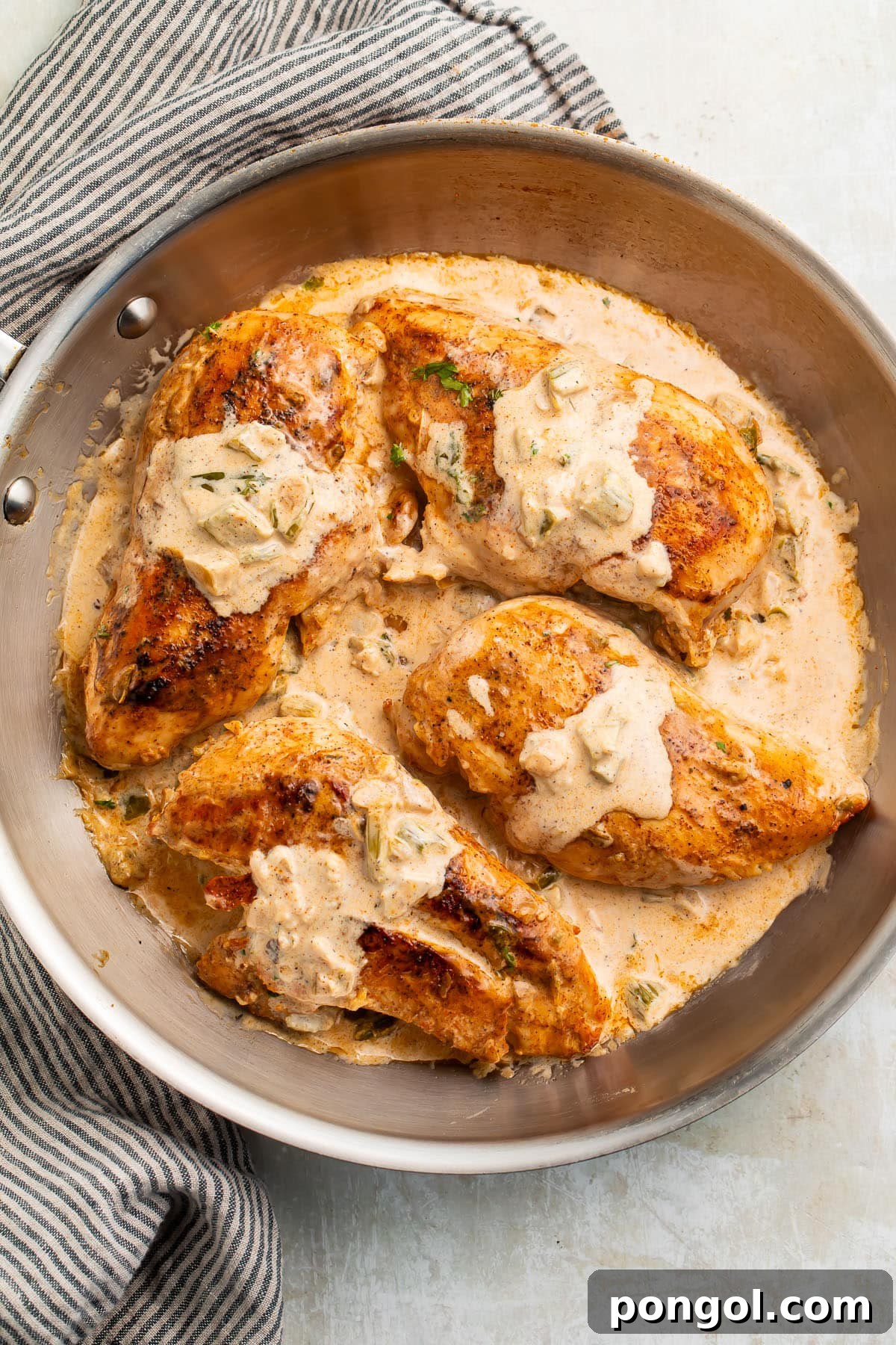 Four seared Cajun-seasoned chicken breasts topped with a creamy sauce in a large silver skillet.