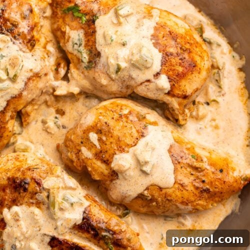 Three seared Cajun-seasoned chicken breasts topped with a creamy sauce in a large silver skillet.