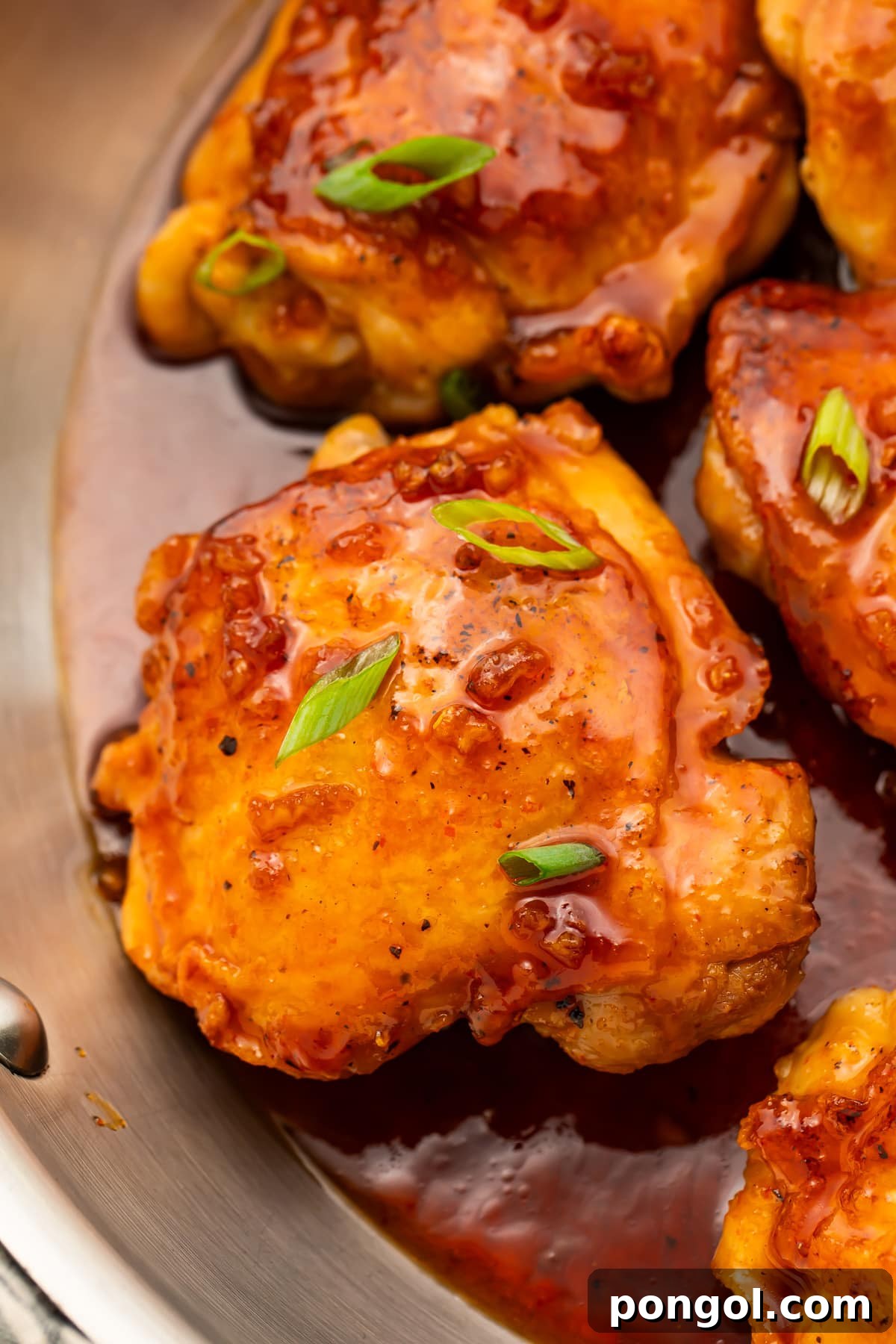 Sriracha Honey Glazed Chicken 2 Honey sriracha chicken thighs resting in a large silver skillet with honey sriracha sauce.