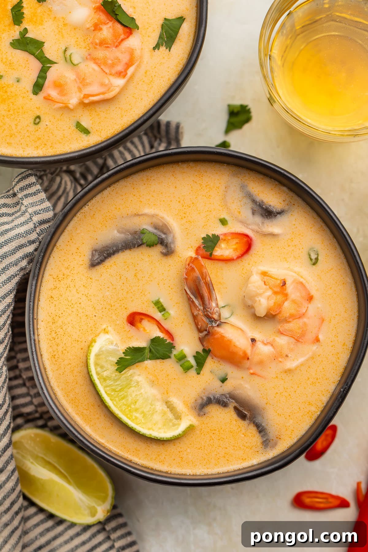 Tom Kha Goong: Creamy Thai Coconut Shrimp Delight 2 An overhead photo of a black soup bowl holding tom kha goong (Thai coconut shrimp soup) with lime wedges, shrimp, and aromatics floating in the broth.