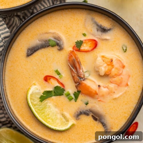 Tom Kha Goong: Creamy Thai Coconut Shrimp Delight 4 An overhead photo of a black soup bowl holding tom kha goong (Thai coconut shrimp soup) with lime wedges, shrimp, and aromatics floating in the broth.