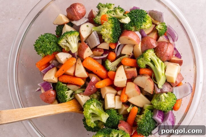 Flavorful One-Pan Chicken Dinner 6 Mixed vegetables in a large glass mixing bowl tossed with oil and salt and pepper.