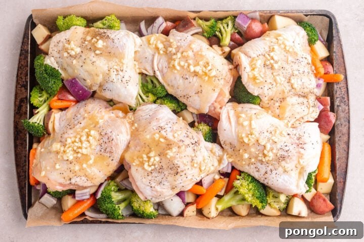 Flavorful One-Pan Chicken Dinner 8 Chicken thighs topped with garlic butter sauce arranged atop a bed of vegetables on a sheet pan.
