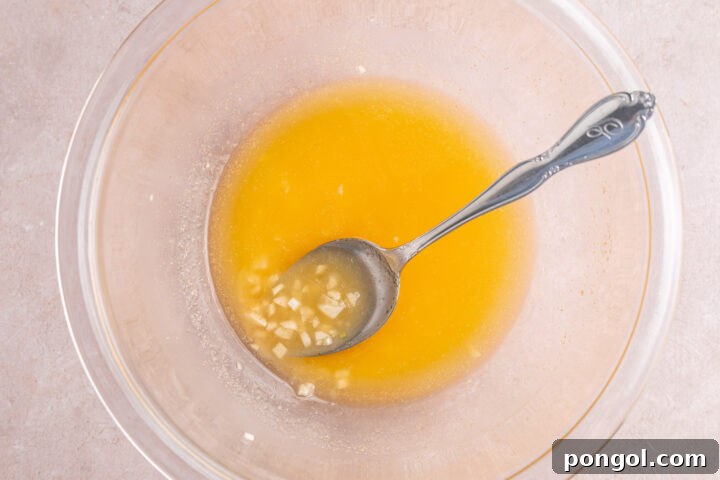 Flavorful One-Pan Chicken Dinner 10 Prepared garlic butter sauce in a large glass mixing bowl with a silver spoon.