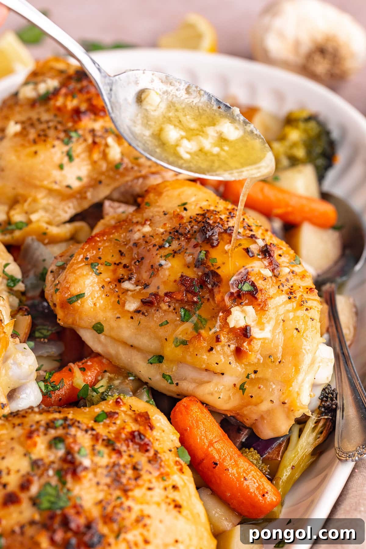 Flavorful One-Pan Chicken Dinner 3 A cook spoons fragrant garlic butter sauce over roasted chicken thighs and oven-roasted mixed vegetables on a sheet pan, ready to return to the oven for finishing.