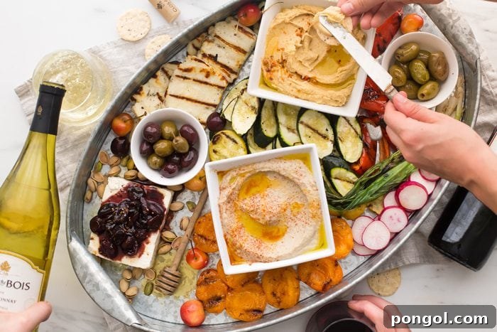 Vibrant healthy Greek appetizer platter with grilled vegetables, halloumi, fresh fruits, and Mediterranean dips arranged for summer entertaining