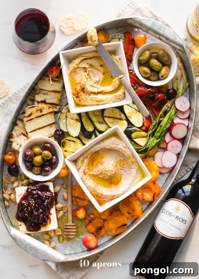 Close-up of a diverse healthy Greek appetizer platter featuring colorful grilled bell peppers, zucchini, halloumi, apricots, and various dips