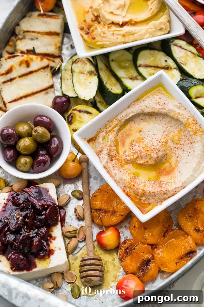 Overhead view of a delicious healthy Greek appetizer platter showcasing grilled halloumi, fresh fruits, colorful vegetables, and creamy dips