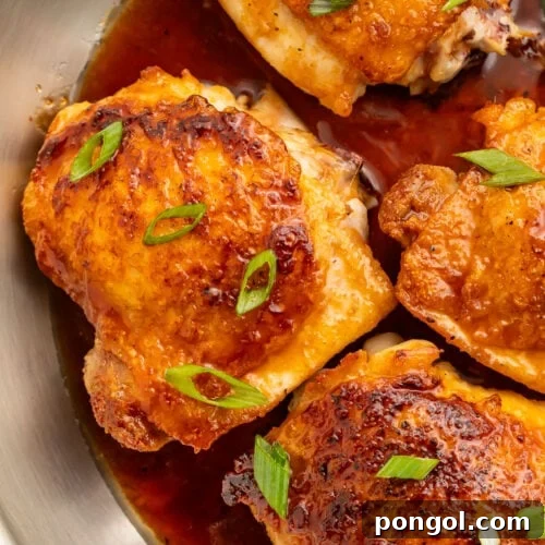 A close-up of bone-in, skin-on chicken thighs in a large silver skillet with a hot honey sauce.