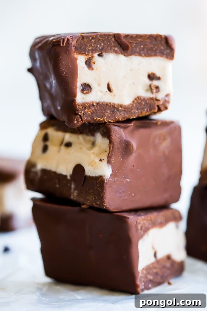 Four healthy vegan ice cream sandwiches on a baking sheet, freshly dipped in chocolate.