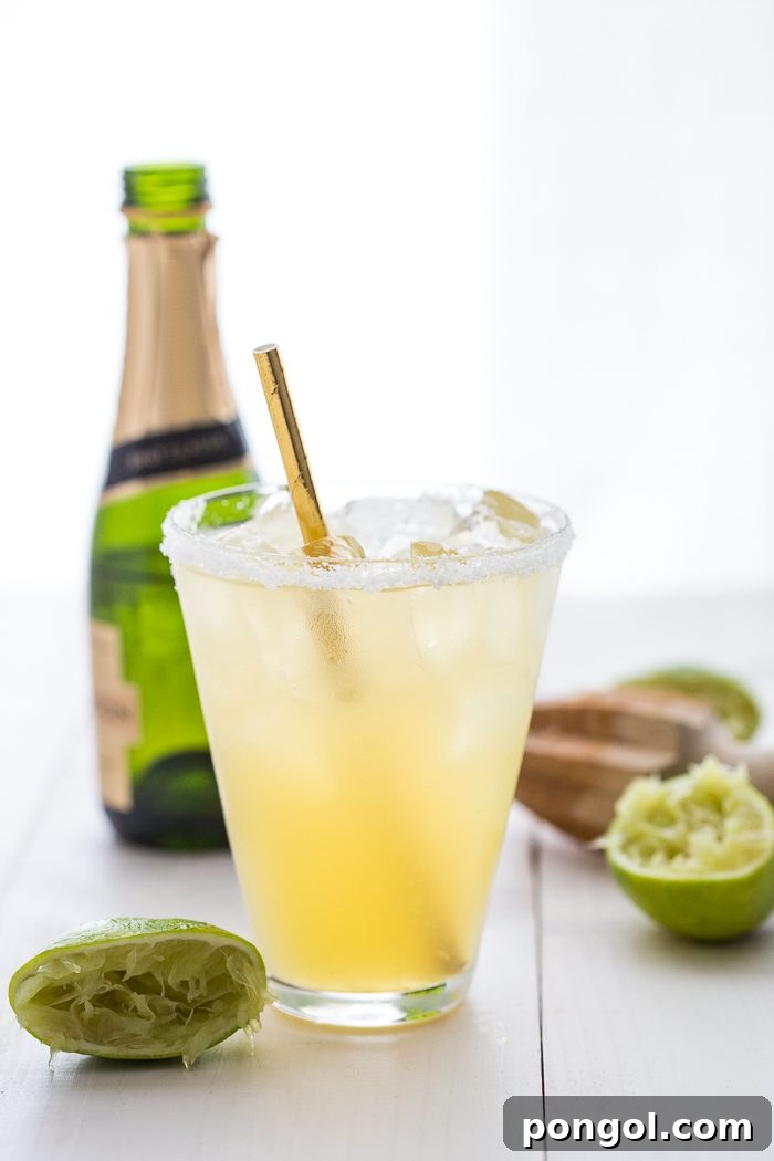 A vibrant Paleo Margarita with a champagne floater, garnished with a lime wedge, sitting on a wooden surface.
