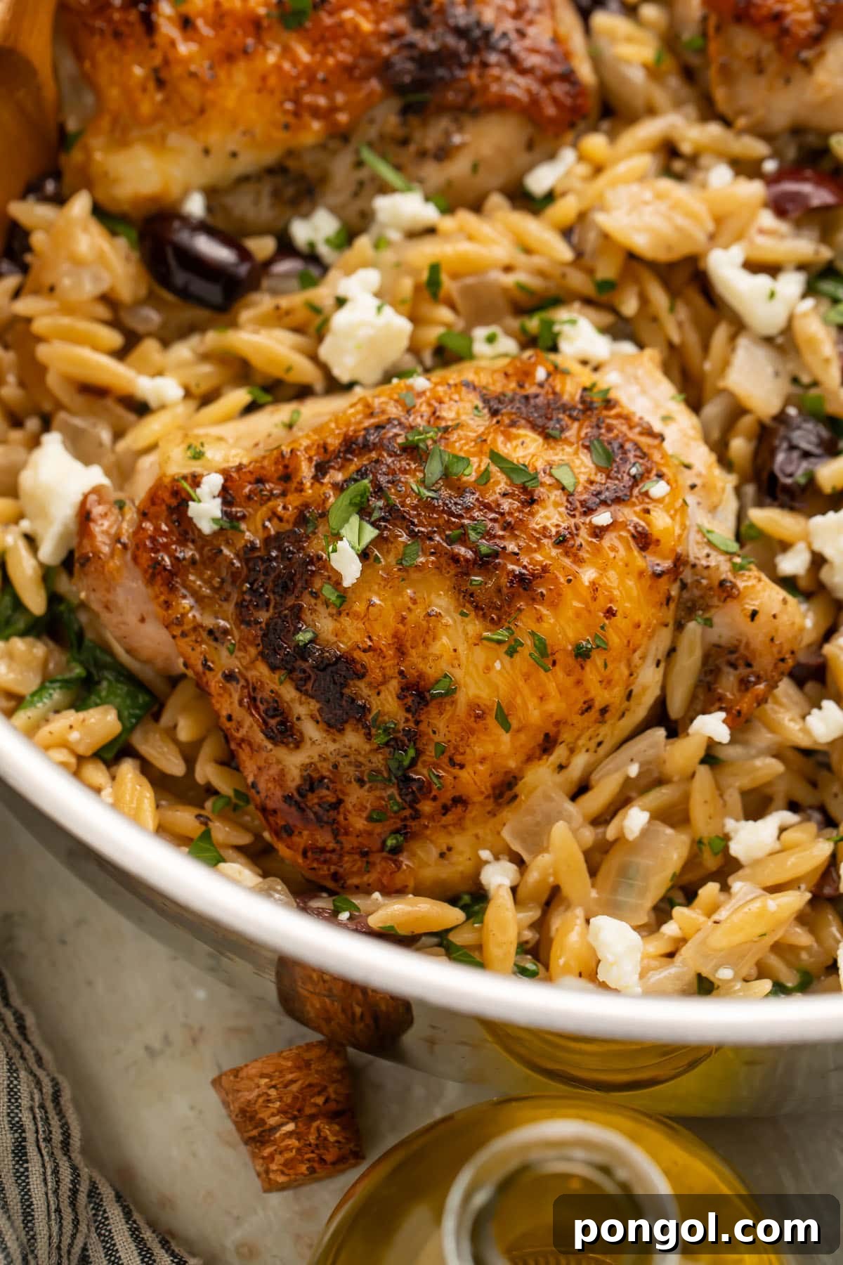 Close-up of a Greek seasoned chicken thigh in a skillet with orzo and feta.