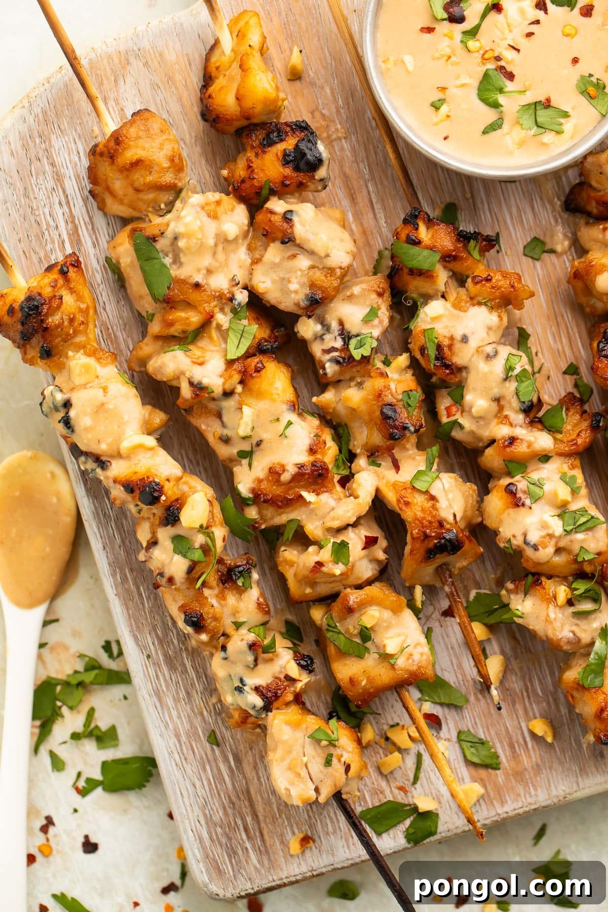 Effortless Chicken Satay with Creamy Peanut Sauce 2 Golden brown chicken satay skewers resting elegantly on a rustic wooden serving board, garnished with fresh cilantro.