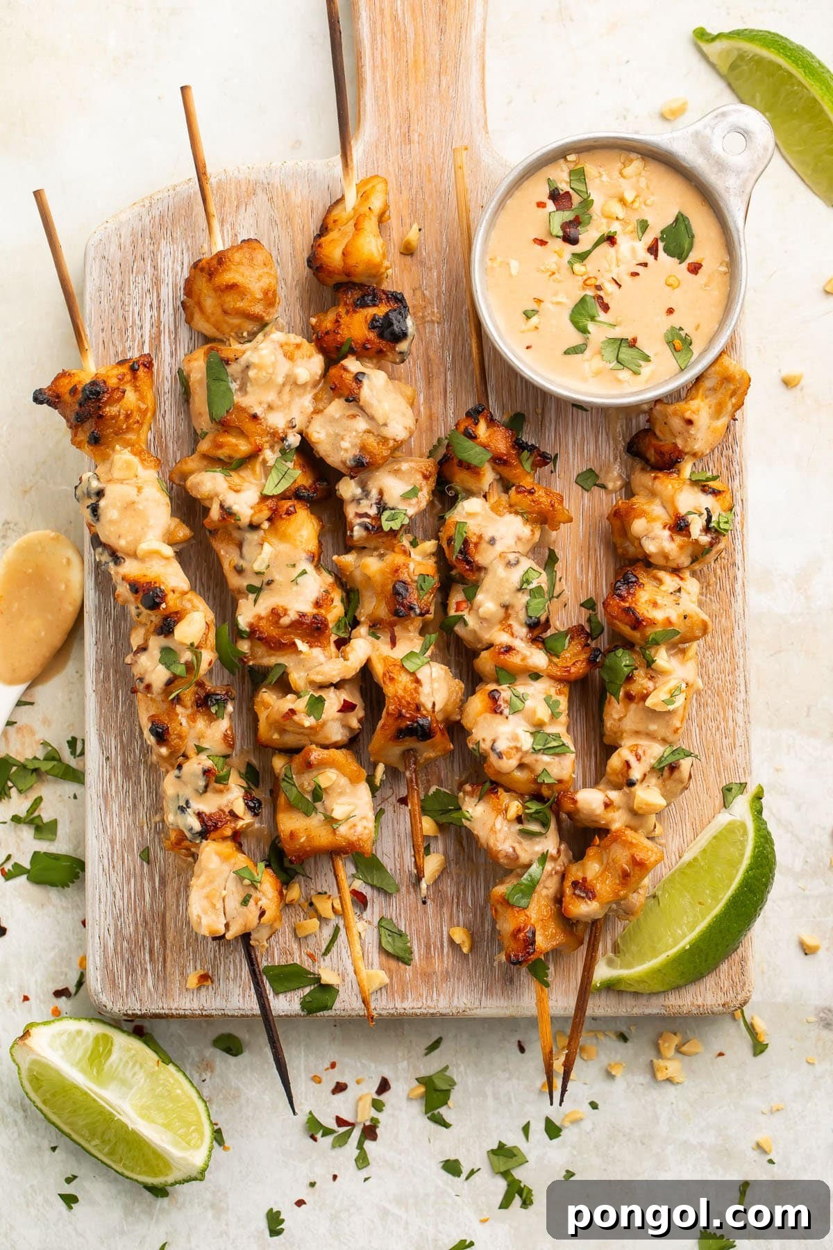Effortless Chicken Satay with Creamy Peanut Sauce 3 Close-up of freshly broiled chicken satay skewers, perfectly charred and glistening with sauce, presented on a wooden board.