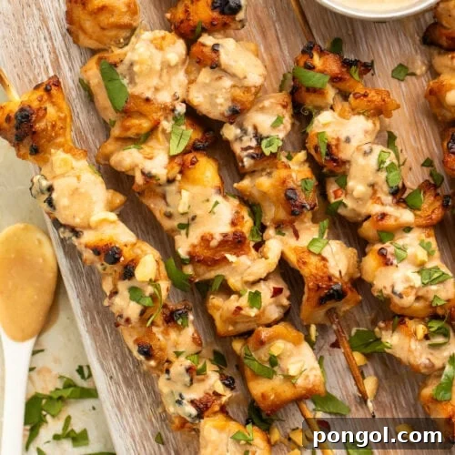 Chicken satay on bamboo skewers resting on a wooden serving board.