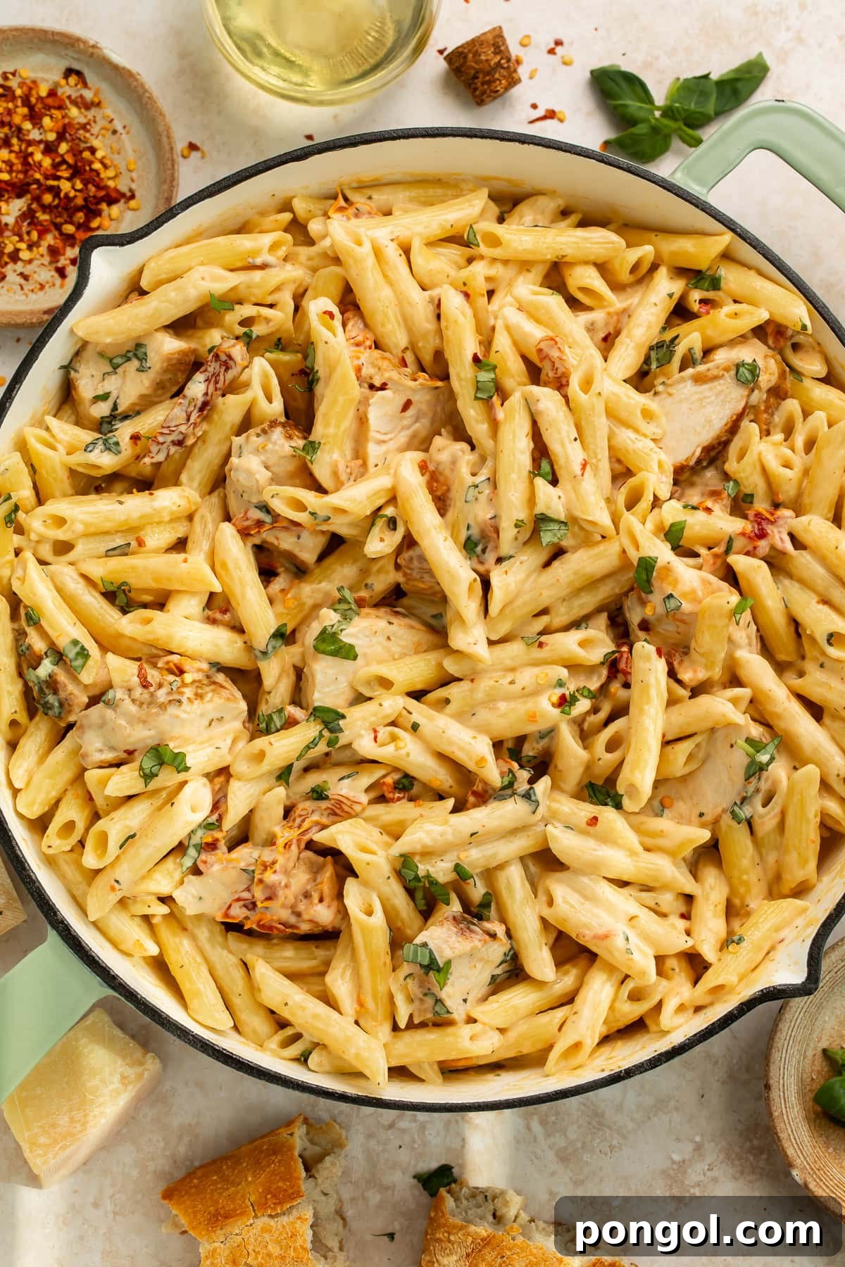 Penne pasta with golden chicken pieces in creamy sun-dried tomato sauce with fresh basil in ceramic serving bowl