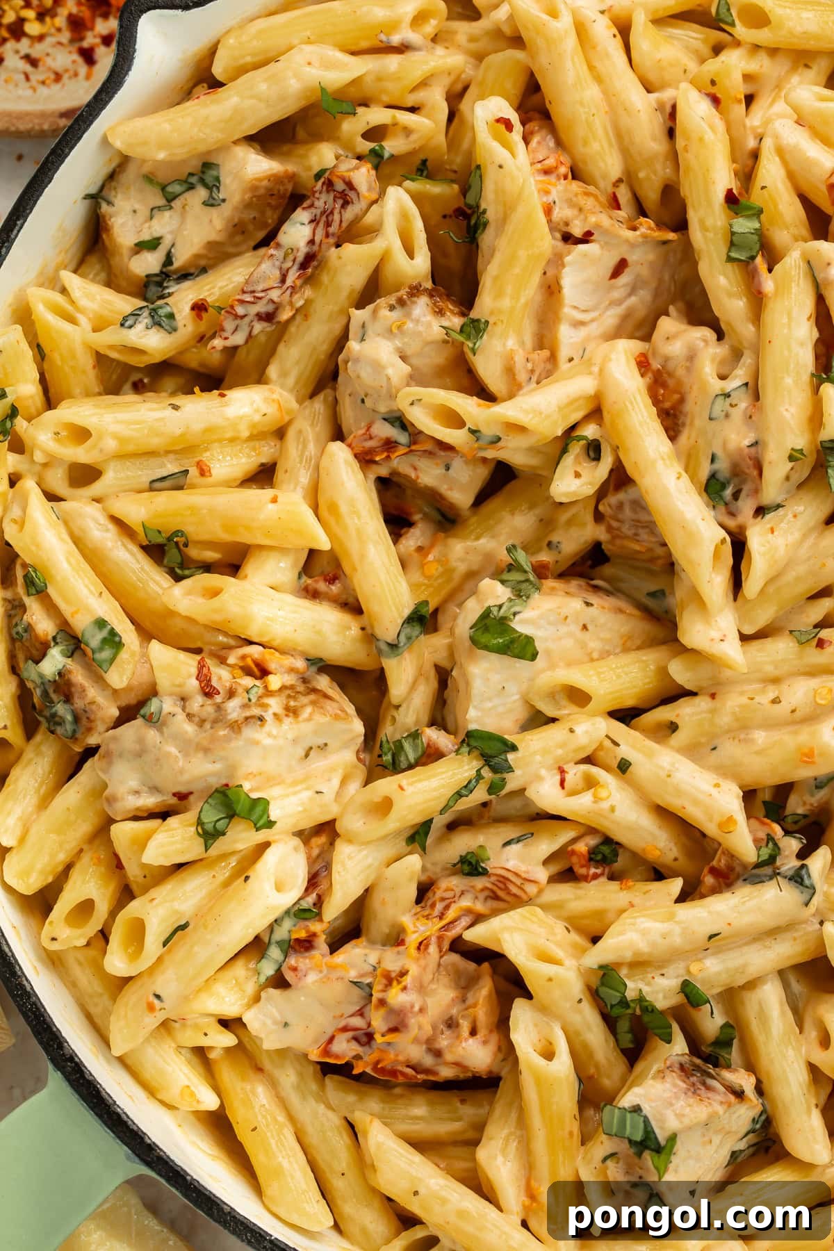 Bowl of marry me chicken pasta garnished with fresh basil and parmesan cheese on dinner table