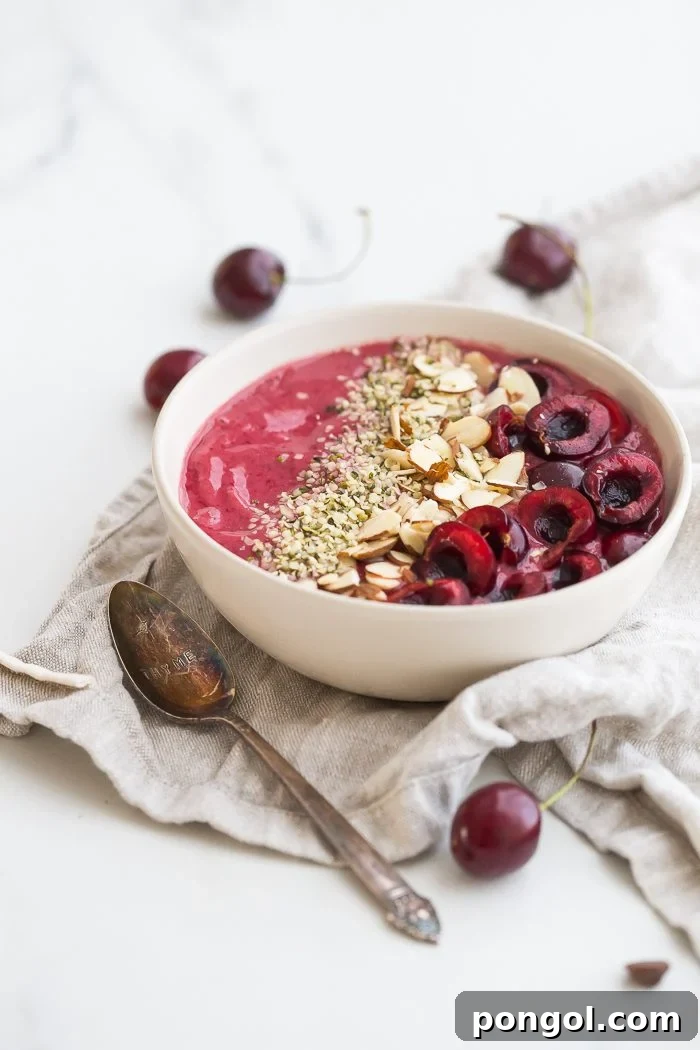 A beautifully arranged cherry smoothie bowl with chia seeds, sliced almonds, and a drizzle of almond butter.